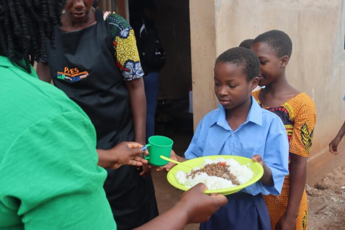 Young boy in blue shirt received plate of food and cup as part of the school meals project implemented by a consortium led by World Vision Mozambique.