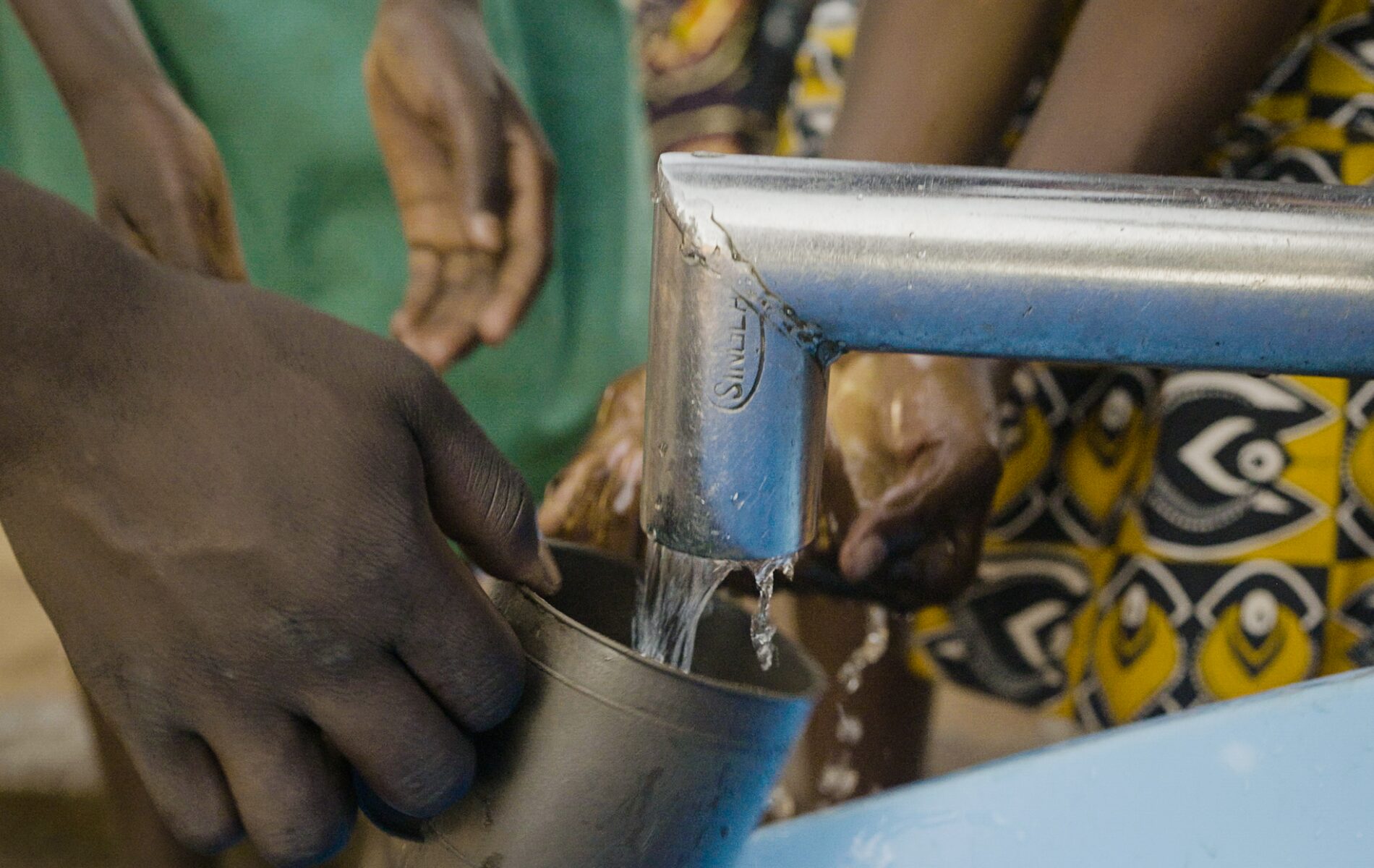 Clean water flows out of a faucet and into a metal cup.
