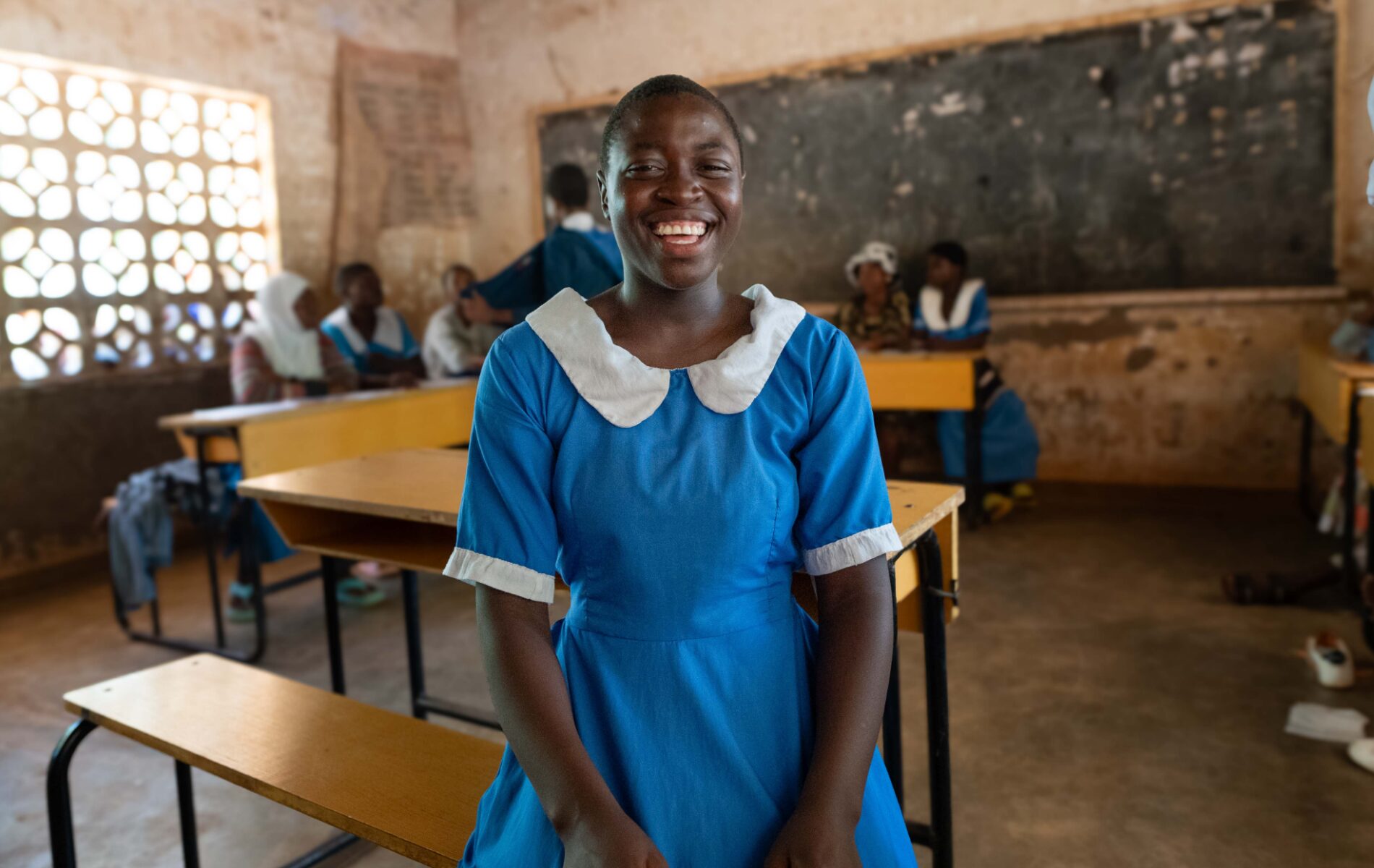 A schoolgirl laughs as she sits on a bench in her classroom.