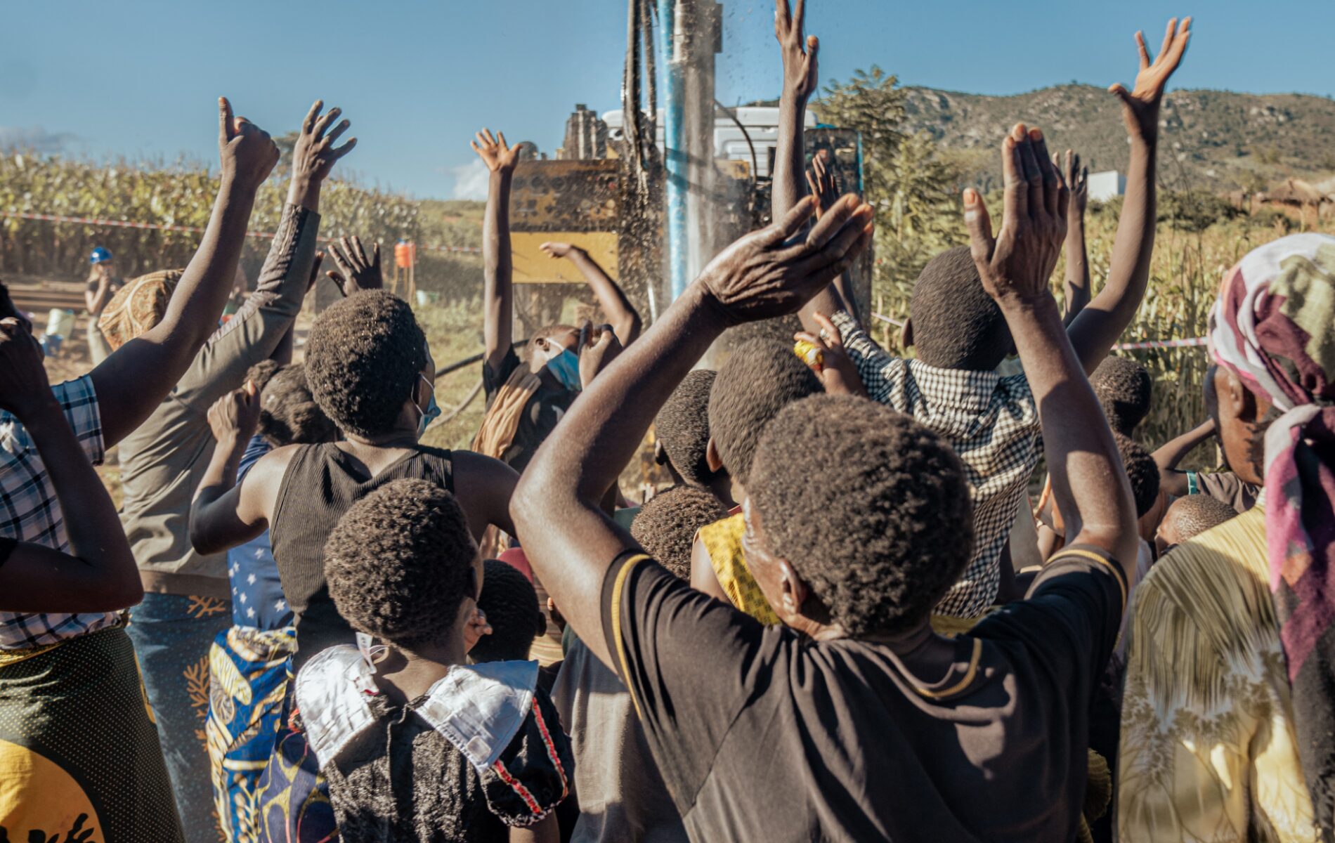 A crowd of people cheer when clean water sprays out of a newly dug borehole.